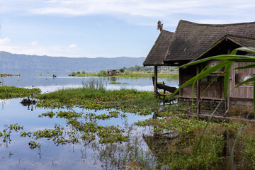 A traditional wooden house sits on the edge of Lake Batur in Bali, Indonesia. Fishermen in small...