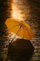 Yellow umbrella lying on wet cobblestone street with golden evening light creating atmospheric moody urban rain scene