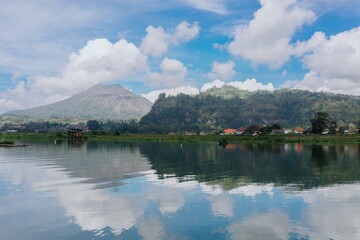 A serene view of Danau Batur in Bali, Indonesia. A local fisherman rows his boat on the calm water,...