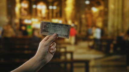Hand holding bangladesh taka banknote indoors with church background, illustrating contrast between...