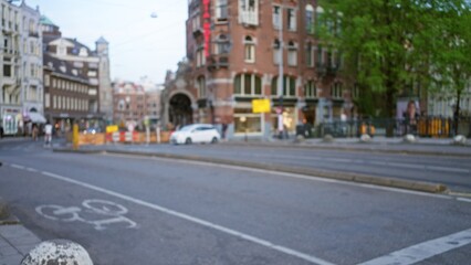 Blurry view of a european city street featuring cyclists and pedestrians showcasing urban architecture in an out-of-focus setting during daytime with a bokeh effect.