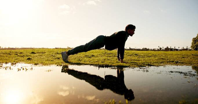 Man, fitness and nature with push ups by lake for workout, arm exercise or physical activity. Active, male person and lifting body weight with reflection by pond for outdoor training or muscle gain