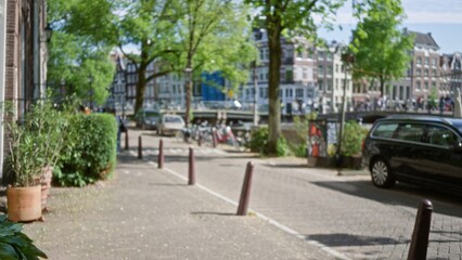Blurred view of a scenic canal street in amsterdam with lush greenery, bicycles, and historic buildings under clear skies, embodying the charming essence of the netherlands.