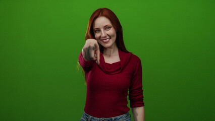 Woman smiling against a vibrant green background, wearing a red sweater and pointing directly at...