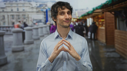 Man steeples fingers while surveying bustling street market stalls during daytime; confidence...