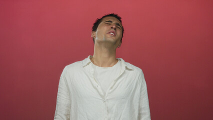 Young man in white shirt stands against red background displaying emotional expression with closed...