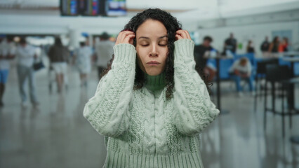 Woman in airport terminal appeared surprised wearing a green sweater with curly hair, hispanic...