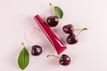 Cosmetic packaging A tube of cherry lip balm lies on a balm sample among ripe cherries. top view....