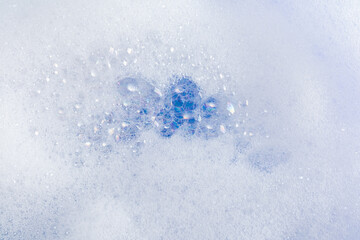 Beautiful foam texture with white fluffy foam waves, clear soap bubbles on the blue water surface. Layout for advertising detergent, cosmetic product.
