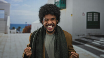 Excited man celebrating against a scenic outdoor coastal background wearing a scarf and expressing...