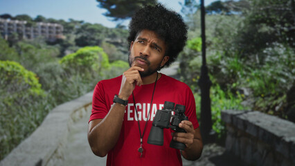 Lifeguard man with binoculars contemplating in a green park setting, surrounded by lush trees and...