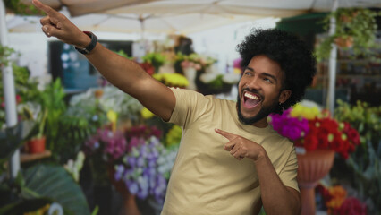 African american man smiling and pointing in an outdoor flower shop in the city, surrounded by...