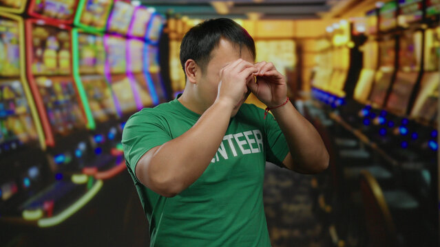 Fototapeta Young man making binocular gesture with hands in vibrant casino surrounded by colorful slot machines evoking playful and whimsical atmosphere indoors
