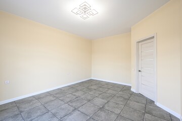 Empty room with beige walls, gray tiled floor, and a modern light fixture. A light wooden door...
