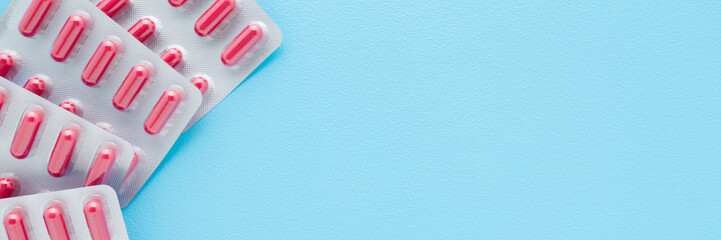 New blister packs of red capsule pills on light blue table background. Pastel color. Wide banner. Closeup. Empty place for text. Top down view. © fotoduets