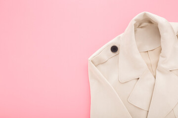 New soft beige coat on light pink table background. Pastel color. Closeup. Female elegant clothes....