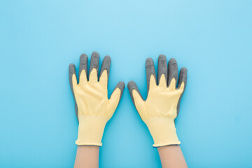 Obraz premium Little child boy hands in new yellow gray protective textile rubber gardening gloves on light blue table background. Pastel color. Closeup. Point of view shot. Top down view.
