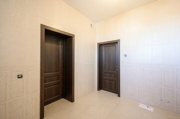 Tiled room with two dark wood doors, cream-colored walls, and a matching tiled floor. Interior,...