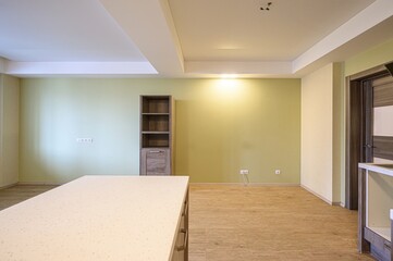 bright, empty room with light green walls and wooden floors. There's a bookshelf and a countertop partially visible
