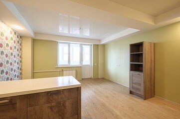 bright, minimalist room with a white ceiling, green walls, and light wood floors. Features include a kitchen island, a bookshelf, and a window with a door