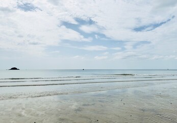 This peaceful coastal scene showcases a quiet beach with gentle waves softly brushing the rippled sand.