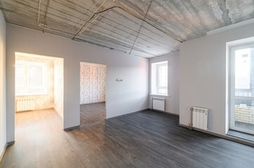 Empty room with bare concrete ceiling, grey walls, wood floor, radiators and windows. Appears unfinished, waiting for final touches