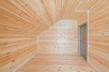 Wooden interior with sloped ceiling, featuring a door, light-colored planks, and electrical wiring