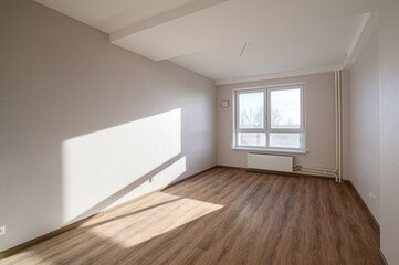 An empty, bright room with wooden flooring, light-colored walls, and a large window letting in...