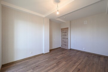 bright, empty room features wood floors, textured walls, and a wooden door. A single bulb hangs from the white ceiling