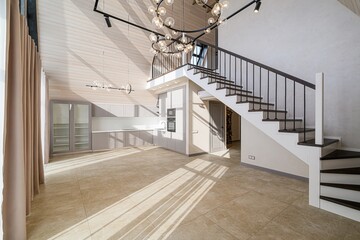 modern, bright interior featuring a staircase, kitchen area, and tiled floor. Sunlight streams in,...