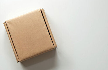 Brown cardboard box on white surface. Fluted top, flap on one side, close-up perspective. Simple, plain, empty space for copy. QR codes printed on shipping label, digital tracking, inventory