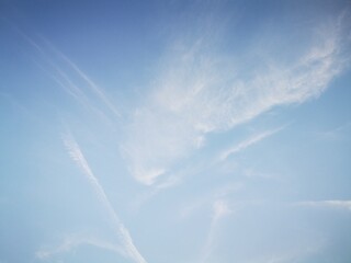 Delicate clouds and vapor trails across a pale blue sky, expressing motion, freedom, and open...