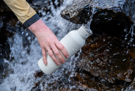 Close-up of hand filling reusable bottle from mountain stream