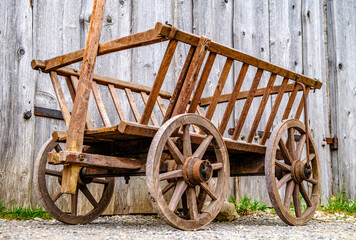 Vintage wooden cart with large wheels resting on a dusty floor in a rustic barn environment during...