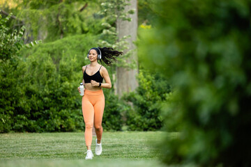 Fit and healthy fitness woman running in the park and enjoying and listening to music.