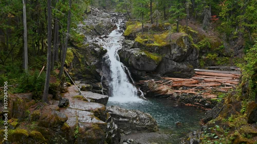 Poster drone view of a small cascading waterfall flowing into a tranquil forest pool surrounded by mossy ro
