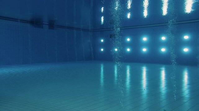 Underwater wide shot of a brightly lit Olympic diving pool, capturing, lights reflections and bubbles.