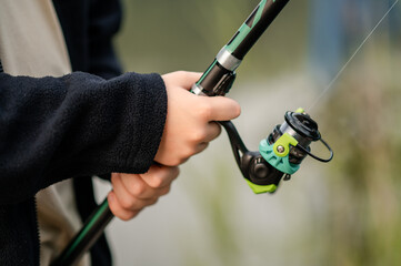 Close-up of teenage boy’s hands holding a fishing rod with a reel, focused and ready for fishing...