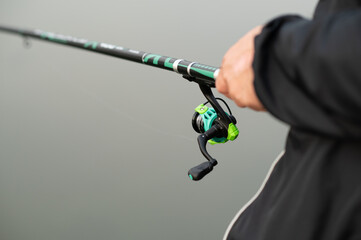 Close-up of adult male hands firmly holding a fishing rod, preparing to cast on a calm lake during...