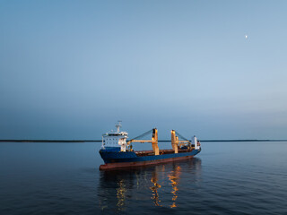 A large cargo ship (bulk carrier) is anchored in the calm waters of the Baltic Sea off the coast of...