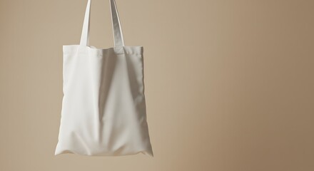 A white tote bag hangs against a soft beige background, showcasing its simple design and texture.