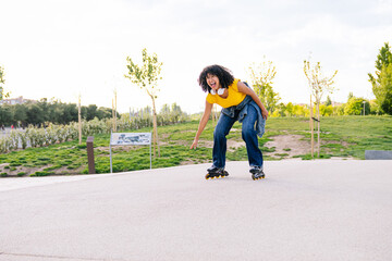 Energetic young woman with headphones roller skating and pointing her finger while enjoying a sunny...