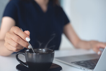 Closeup, woman working on laptop computer, hand holding a cup of coffee on office table. remote work, online job, freelance lifestyle