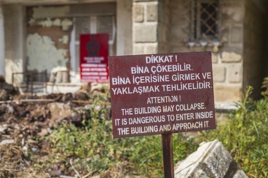 Varosha, Cyprus - 25 June 2025: View of a weathered warning sign standing starkly against a dilapidated building, its crumbling facade a silent testament to time and neglect.