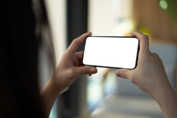 Mockup, horizontal black smartphone with blank white screen. Woman hand holding mobile phone in horizontal l position, watching blank copy space screen for video content or website advertisement