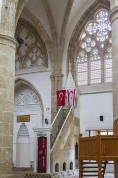 Varosha, Cyprus - 25 June 2025: View of Lala Mustafa Pasha Mosque's interior, where aged stone pillars meet modern white walls, adorned with the Turkish flag, under the elaborate stained-glass window.