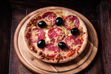 Pizza with salami, mozzarella and cheddar cheese. Wooden background. Soft focus. Close up.	