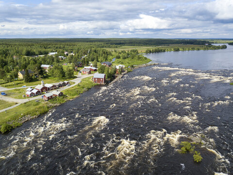 Aerial view of the Torne River's powerful rapids contrast with the serene village of Kukkolaforsen, blending raw nature with human settlement, Haparanda, Norrbotten County, Sweden.