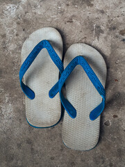 A pair of worn blue flip-flops placed on a rough concrete floor, symbolizing simplicity and daily...