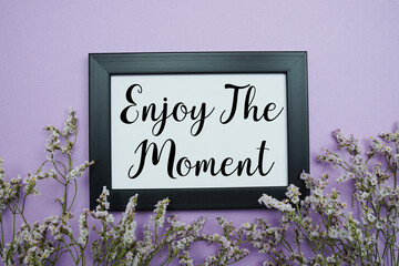Enjoy The Moment text with flowers bouquet decoration on purple background